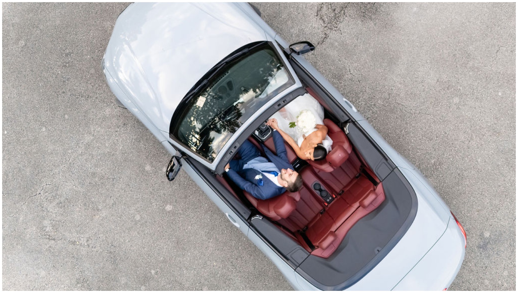 A look down onto newlyweds holding hands in a luxury convertible with red seats