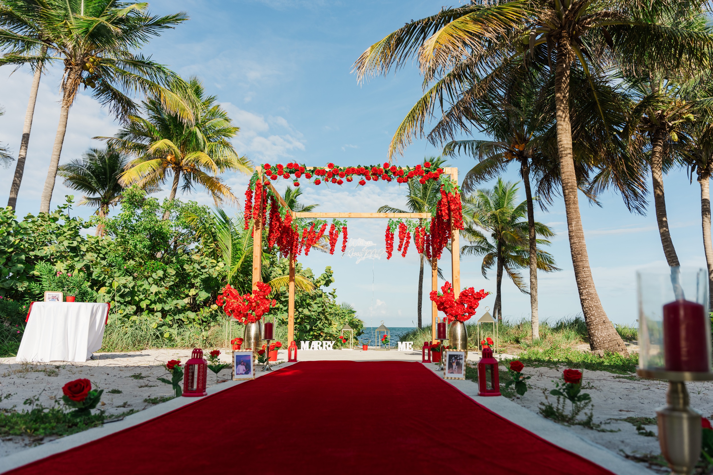 A view of a wooden arbor draped in red flowers on a beach for a proposal Miami