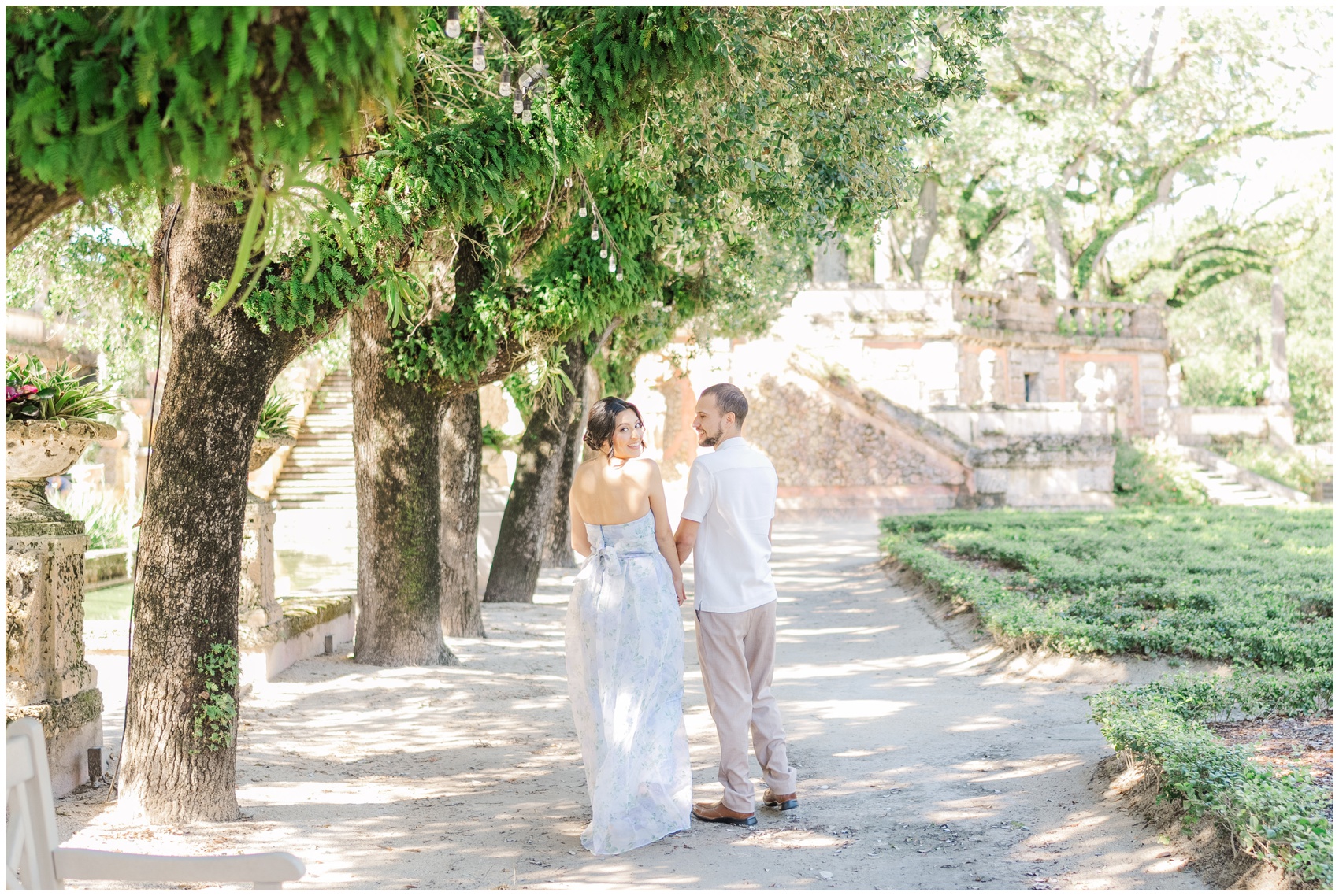 A bride smiles over her shoulder while exploring elaborate gardens