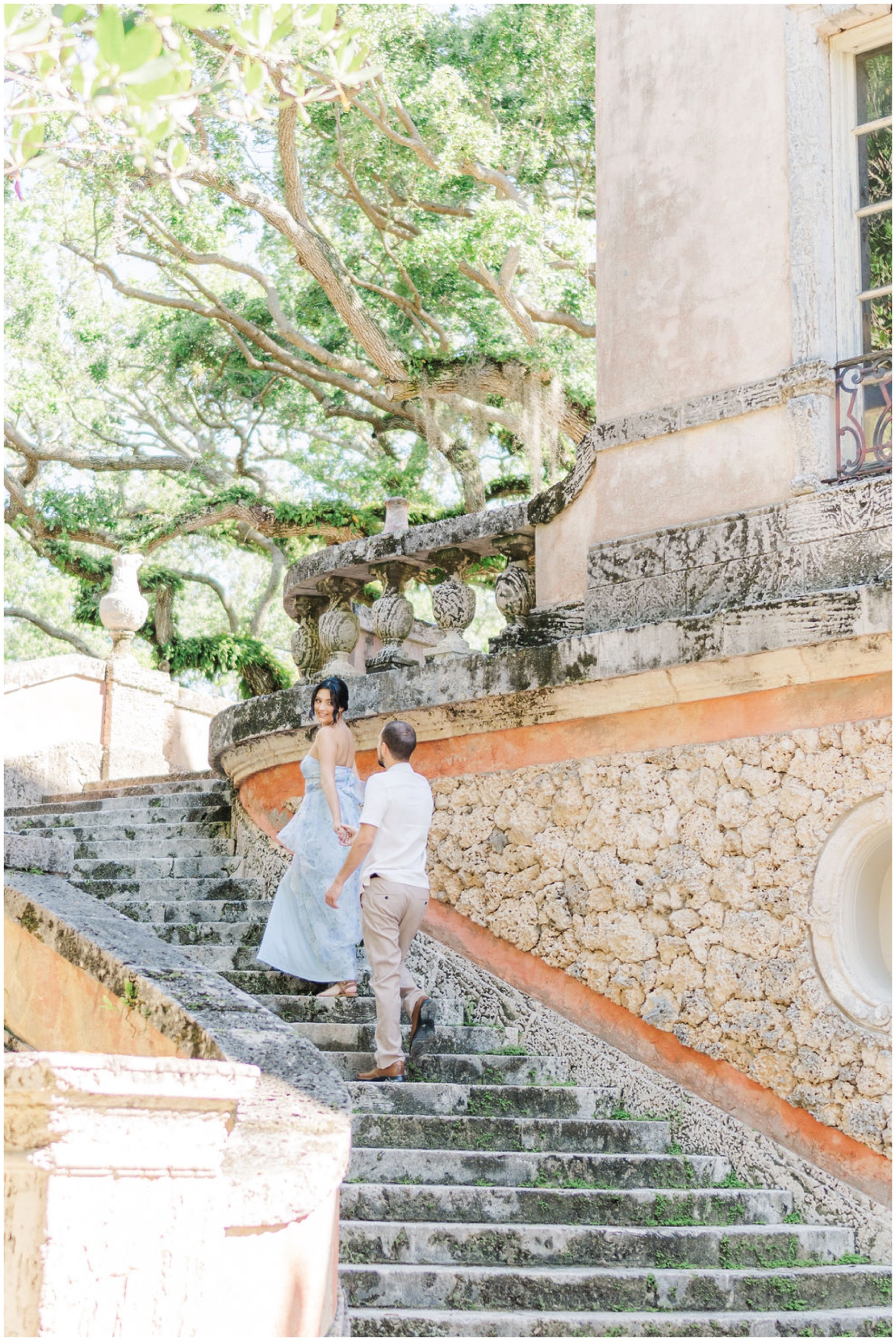 Newlyweds hold hands and walk up limestone stairs in the gardens of one of the luxurious wedding venues in Miami