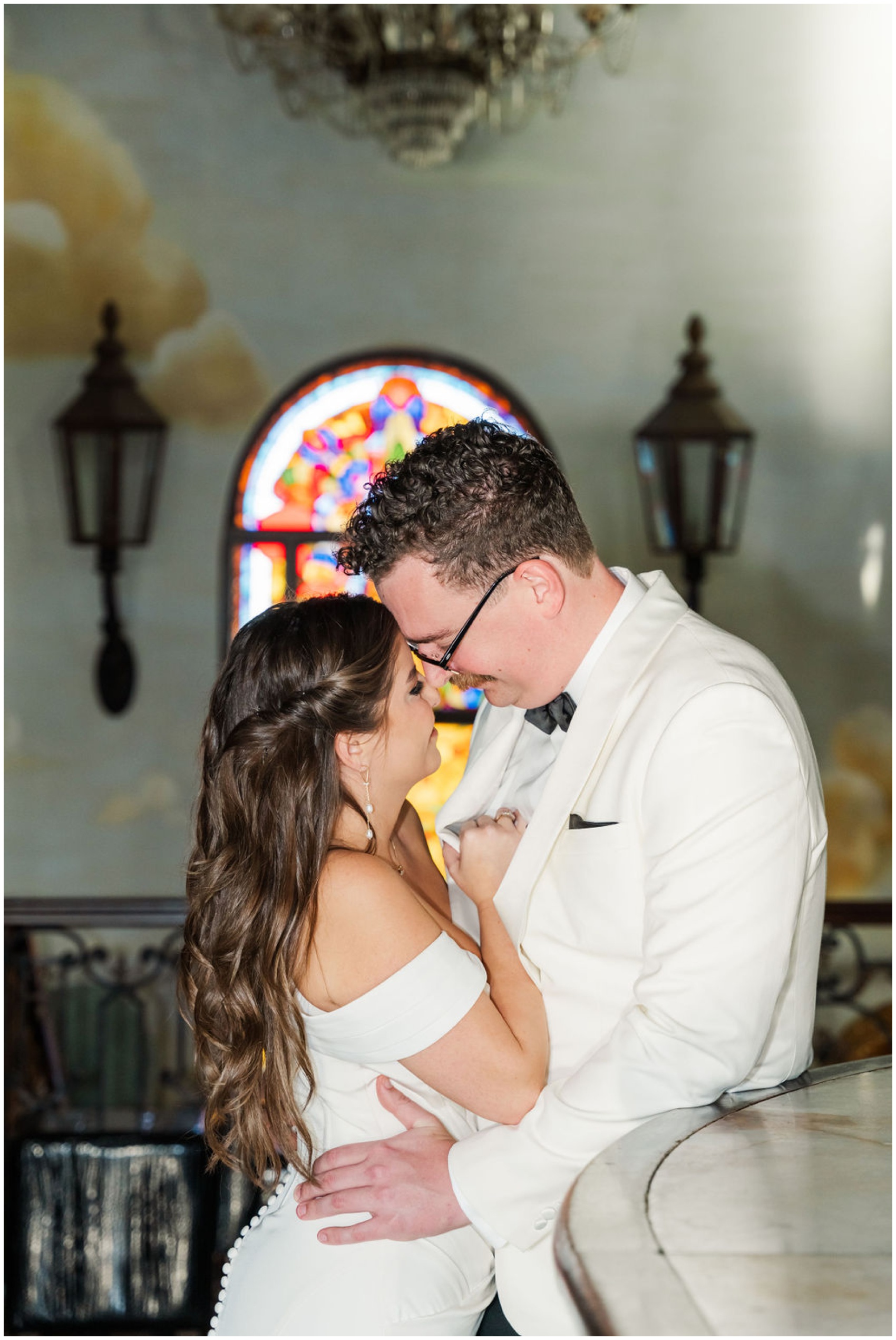 Newlyweds snuggle while leaning against a bar in an ornate venue