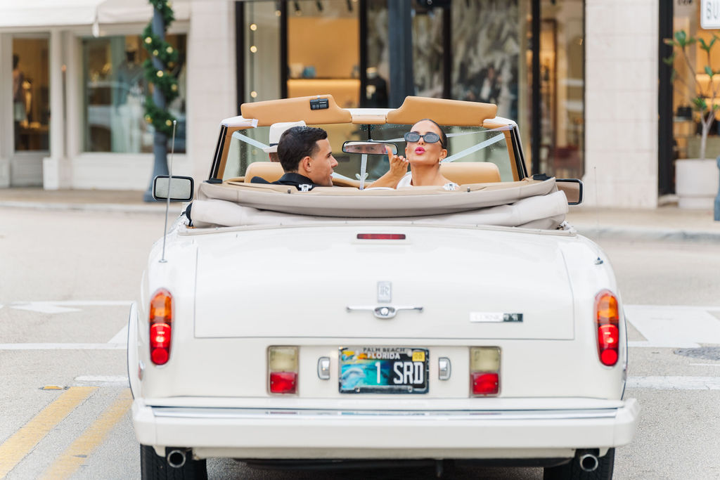 A bride blows a kiss from a vintage convertible while leaving one of the wedding venues in west Palm Beach