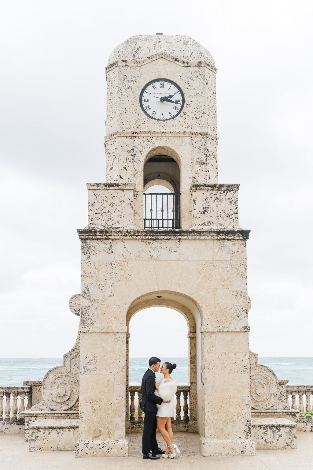 A bride and groom lean in for a kiss under a clock tower at one of the wedding venues in west Palm Beach