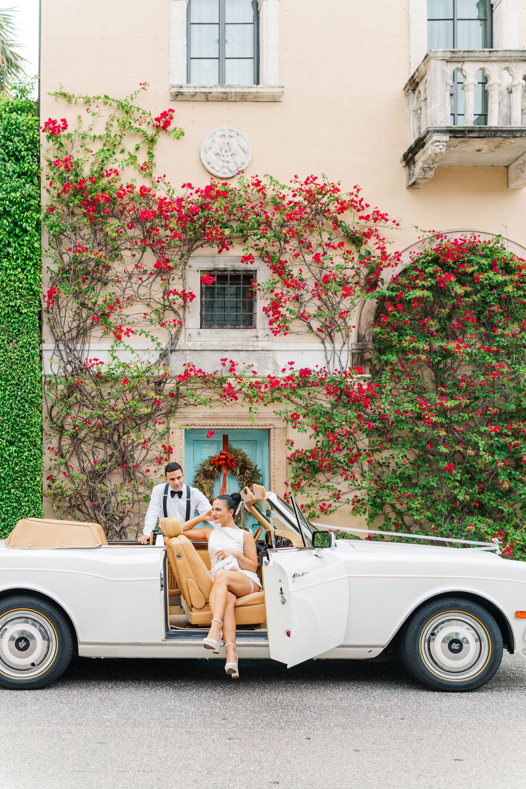 Newlyweds hang out in a vintage car in front of a flower vine covered spanish style building