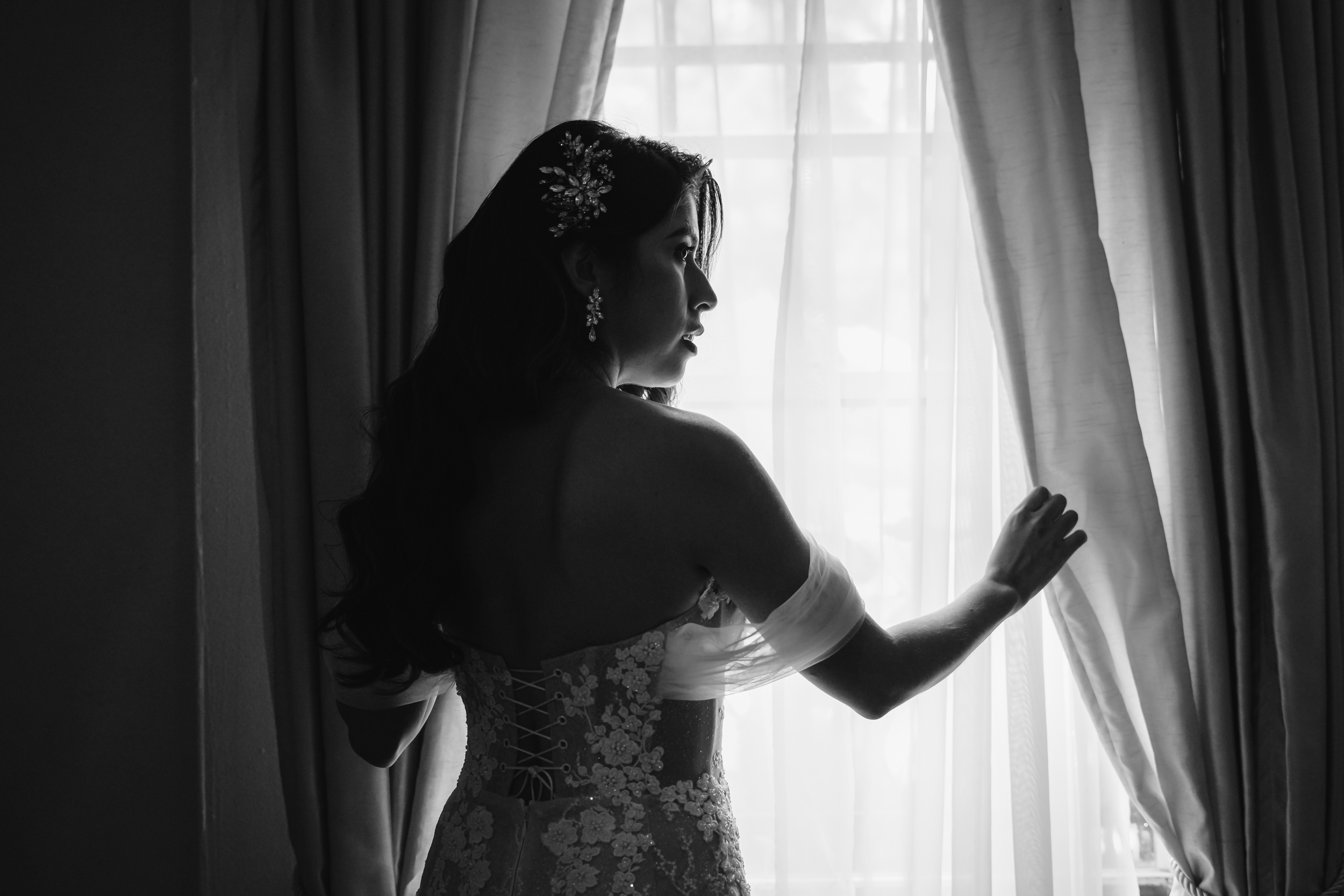 A bride peaks out the window in her dress in black and white