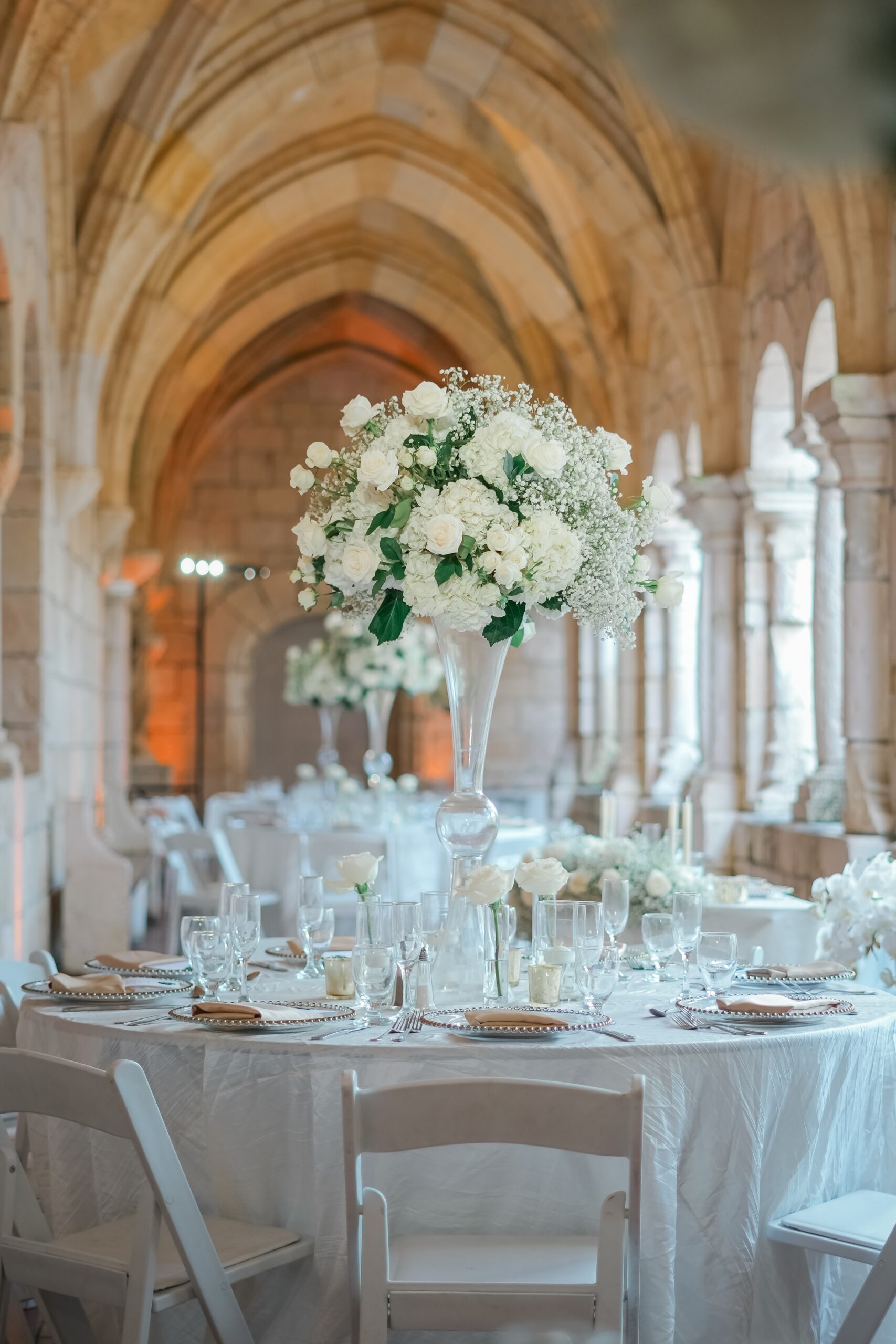 A wedding reception table set up in a colonnade with white linen and tall floral centerpiece at an Ancient Spanish monastery wedding