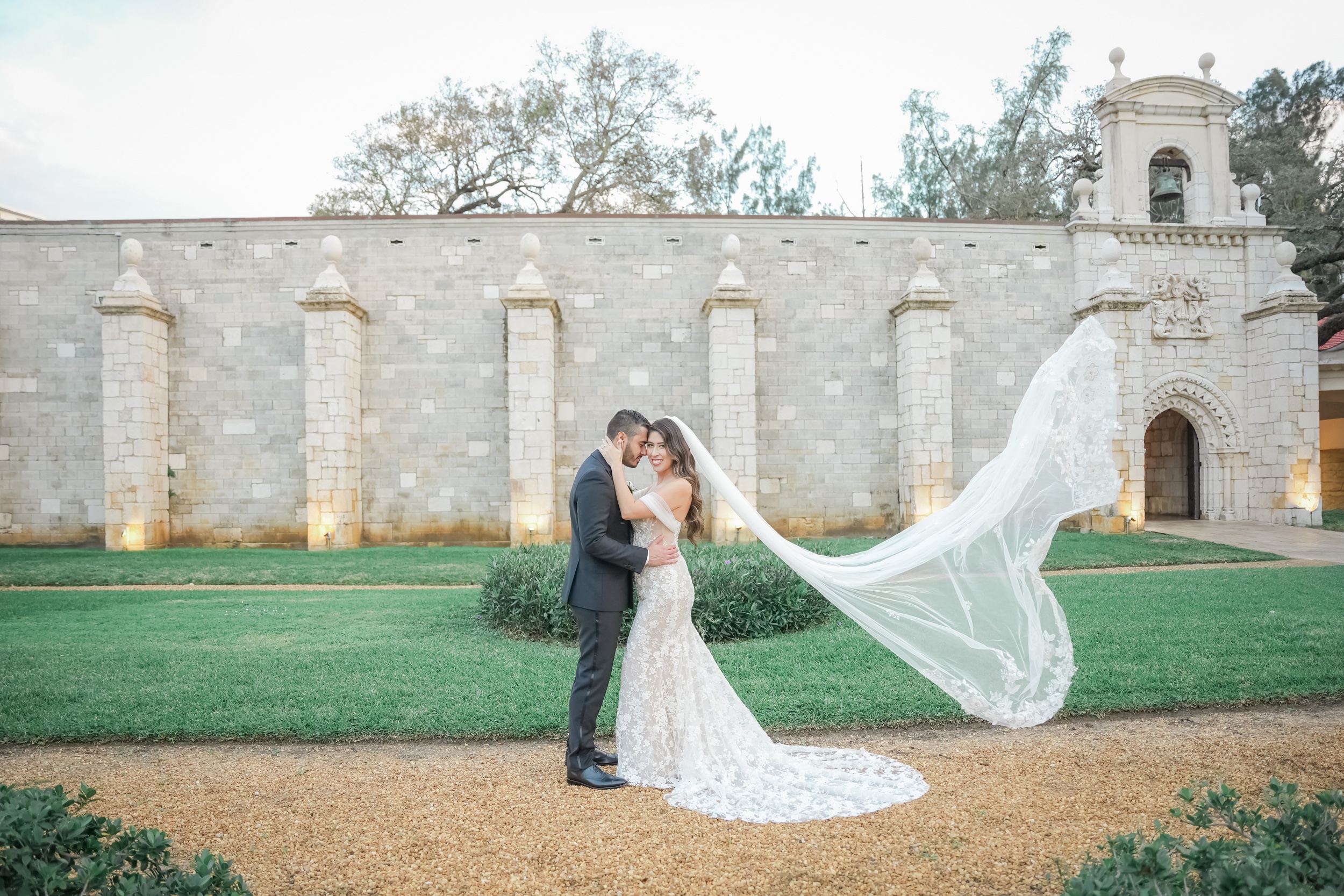 A bride smiles as her veil flies in the wind behind her outside their Ancient Spanish monastery wedding