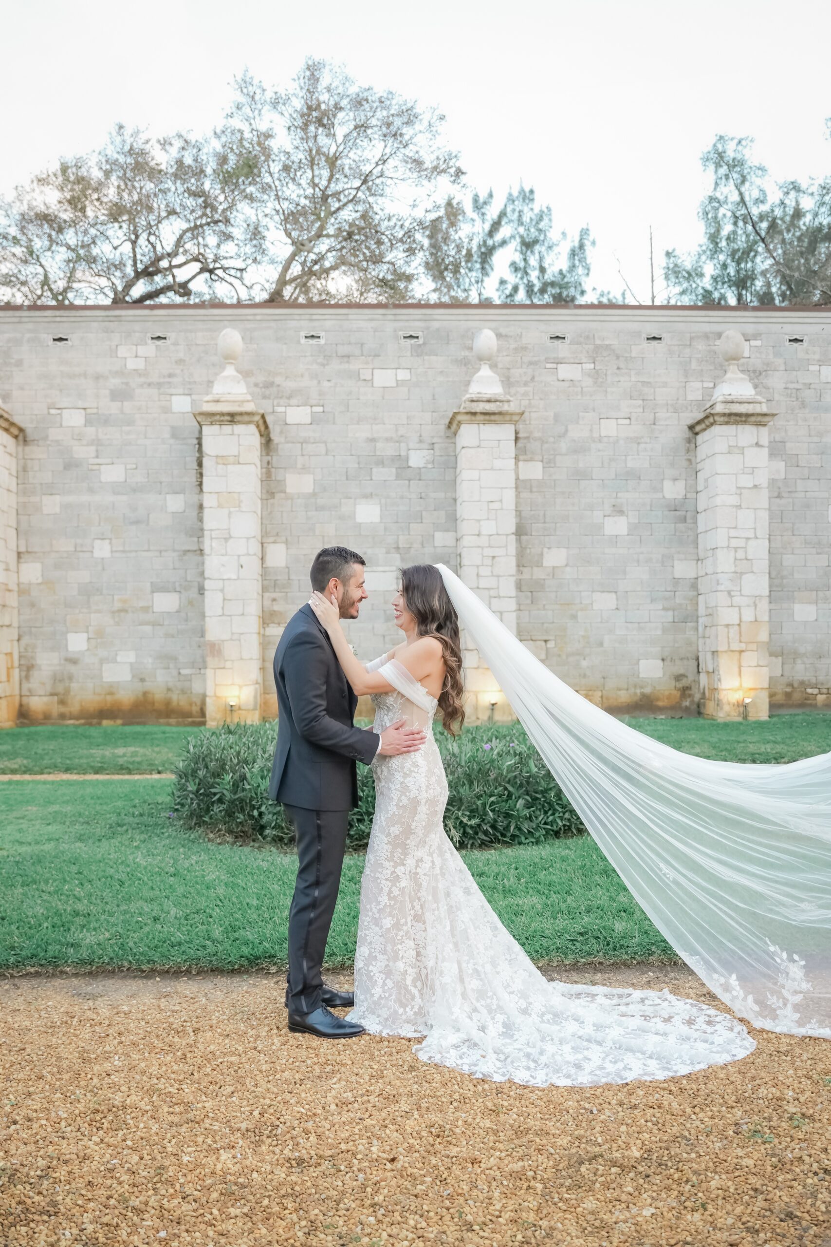 A bride and groom hug and smile at each other in the gardens of the Ancient Spanish monastery wedding venue