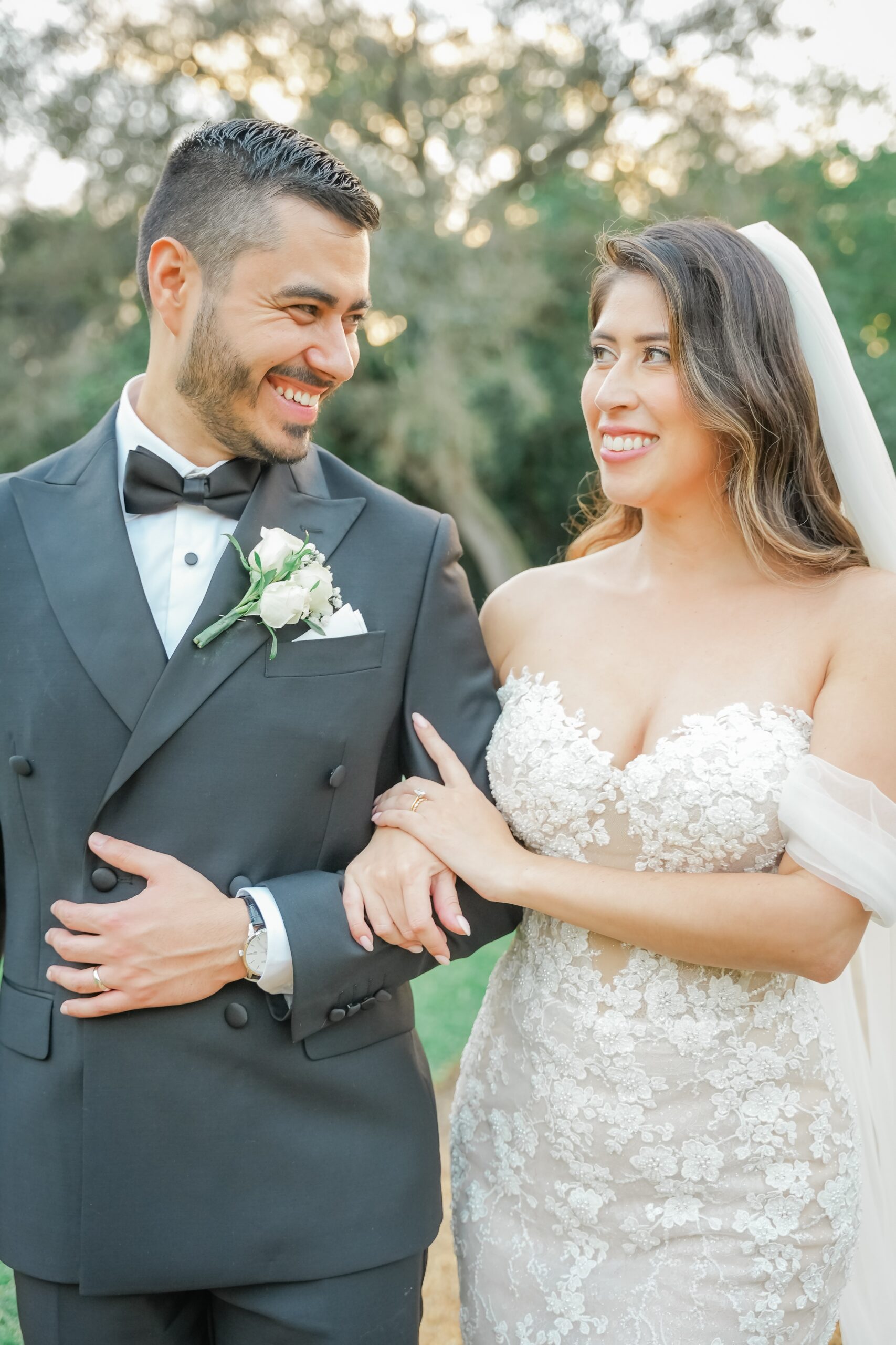 Newlyweds laugh while walking in a garden at sunset with arms locked