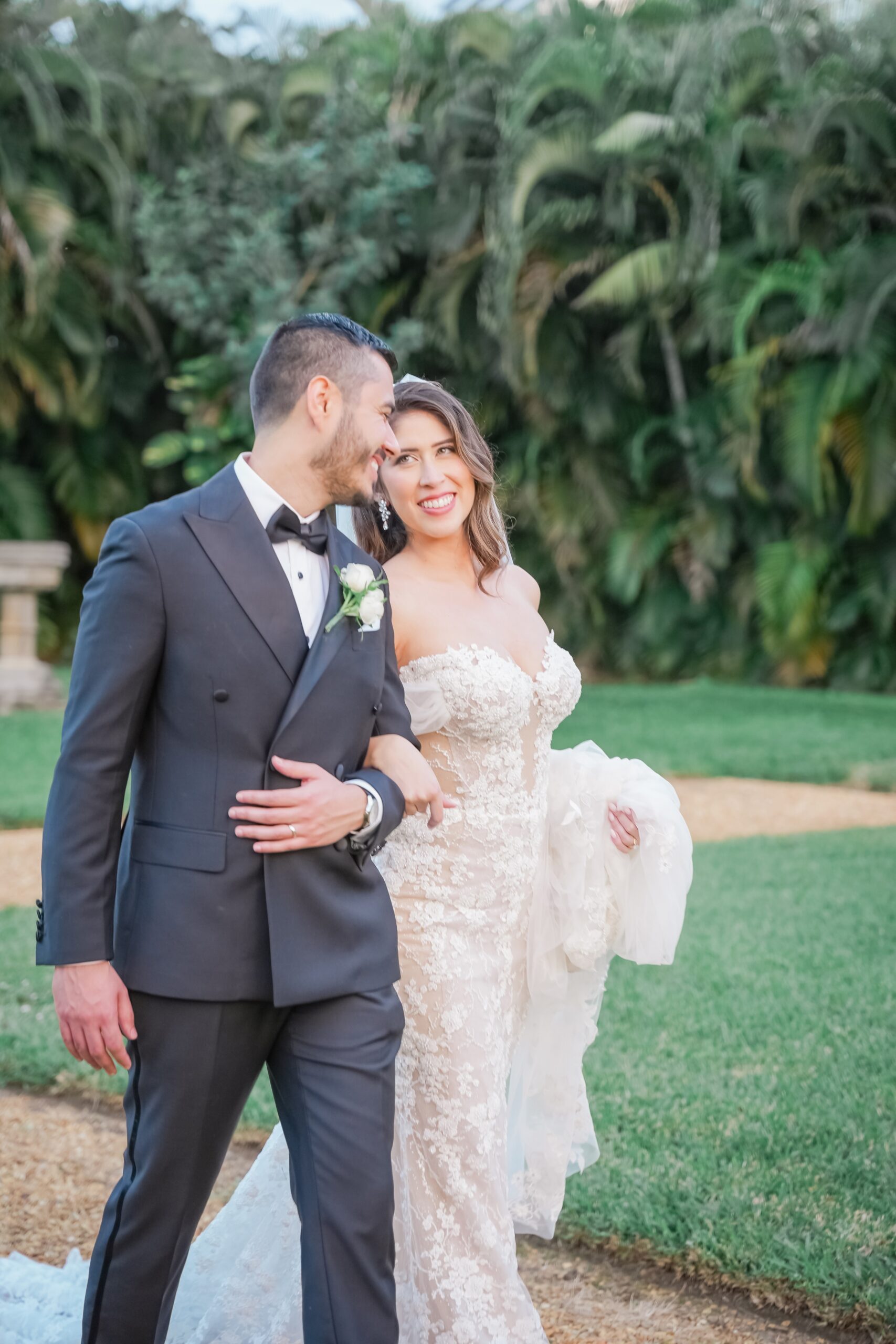 A bride and groom giggle while walking arm in arm through a garden path