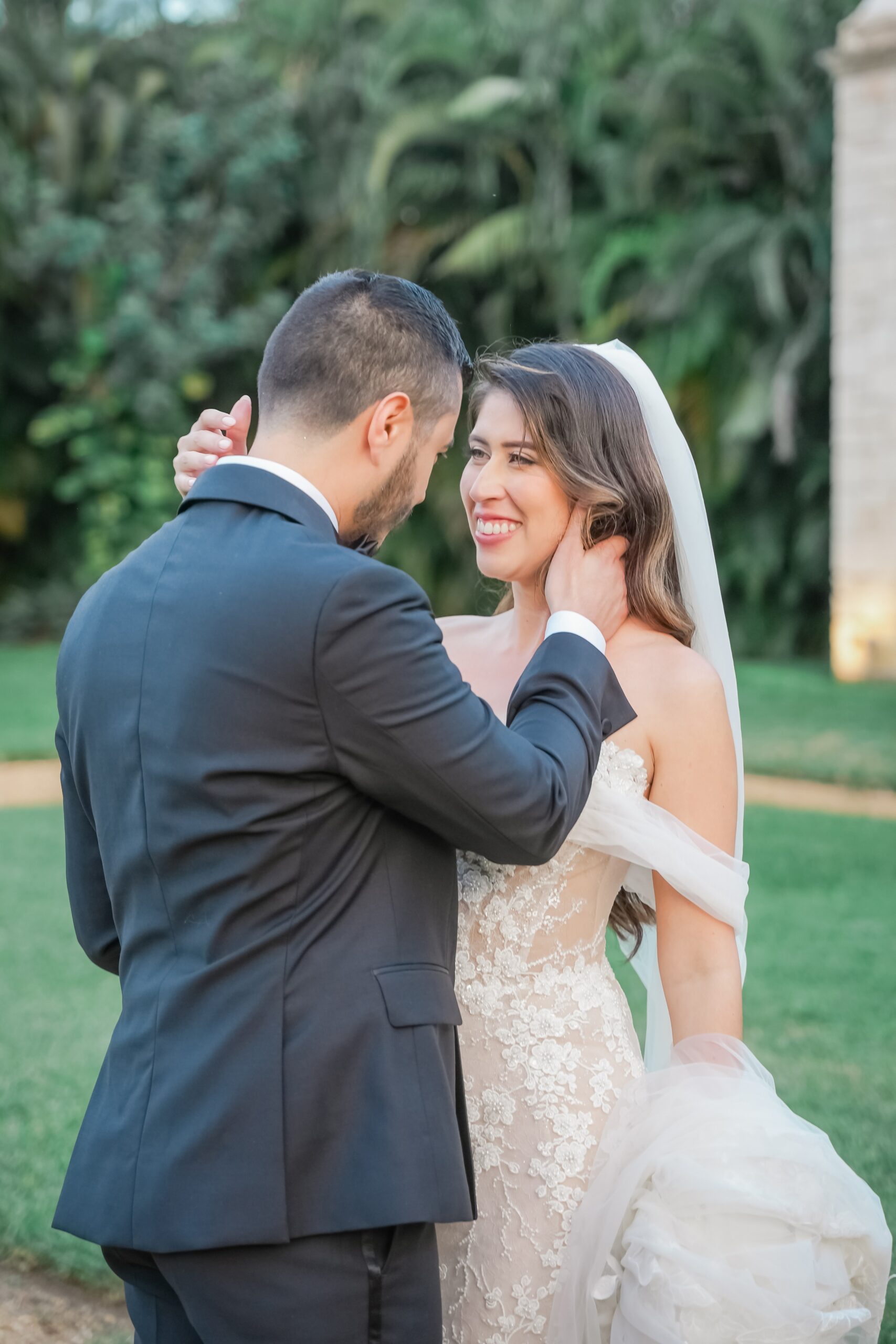 Newlyweds lean in for a happy kiss in the gardens in a black suit and lace dress