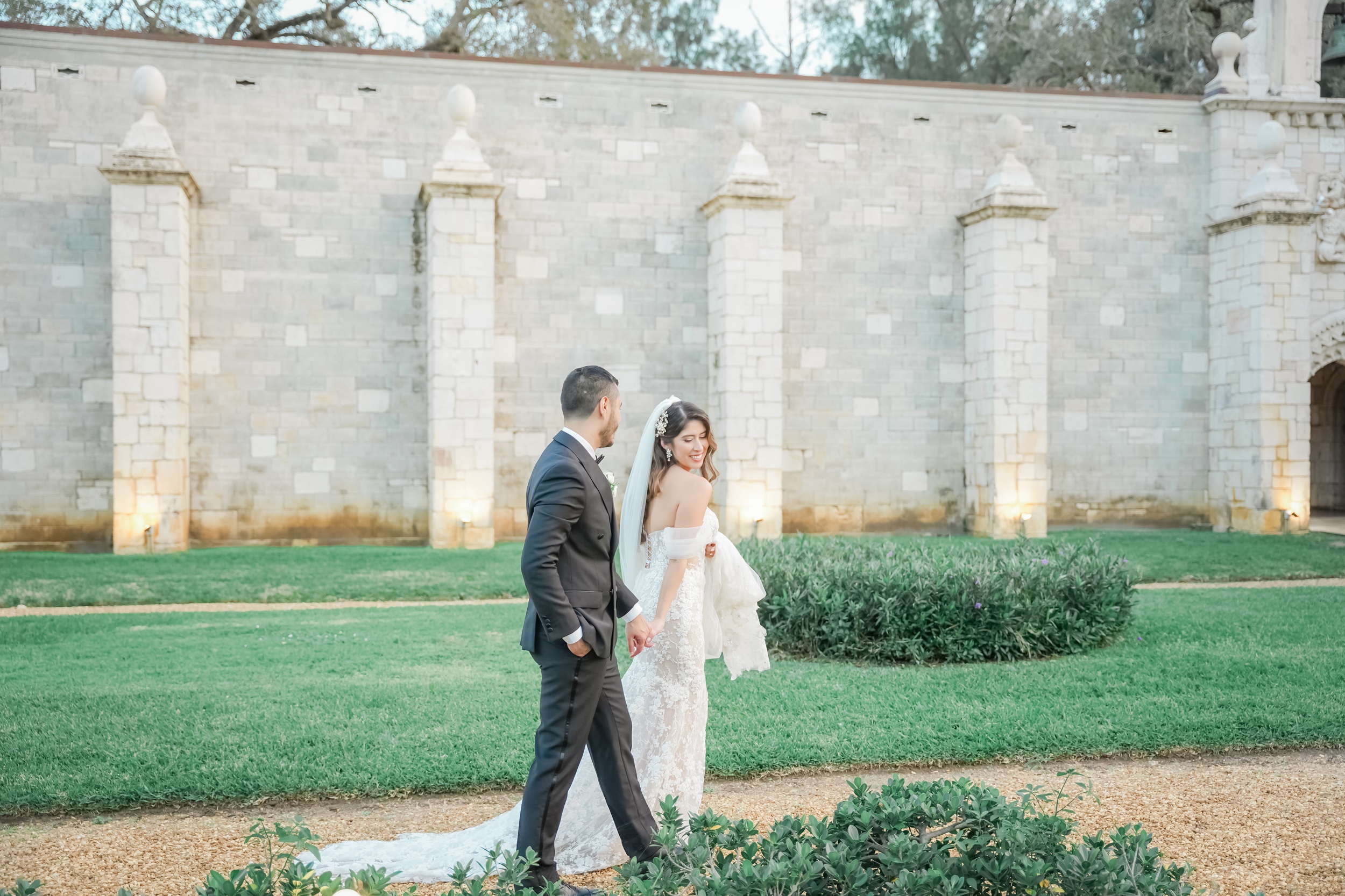 A bride and groom hold hands while walking the grounds of their Ancient Spanish monastery wedding