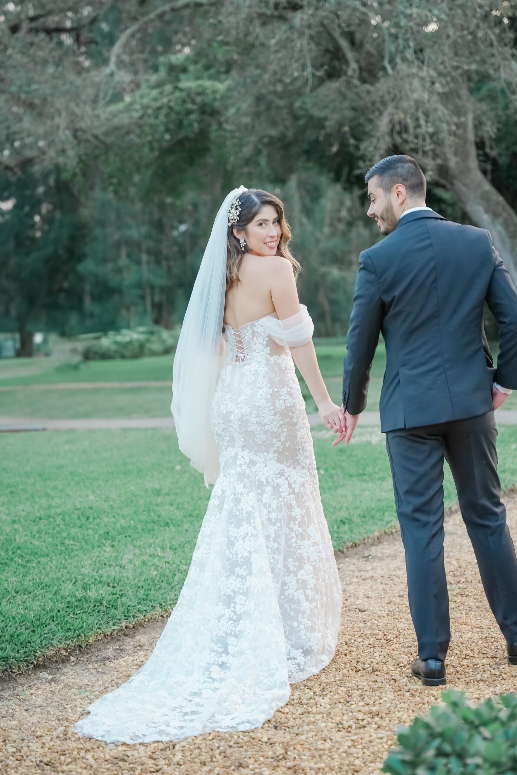 Newlyweds walk on a garden path as the bride smiles over her shoulder at their Ancient Spanish monastery wedding