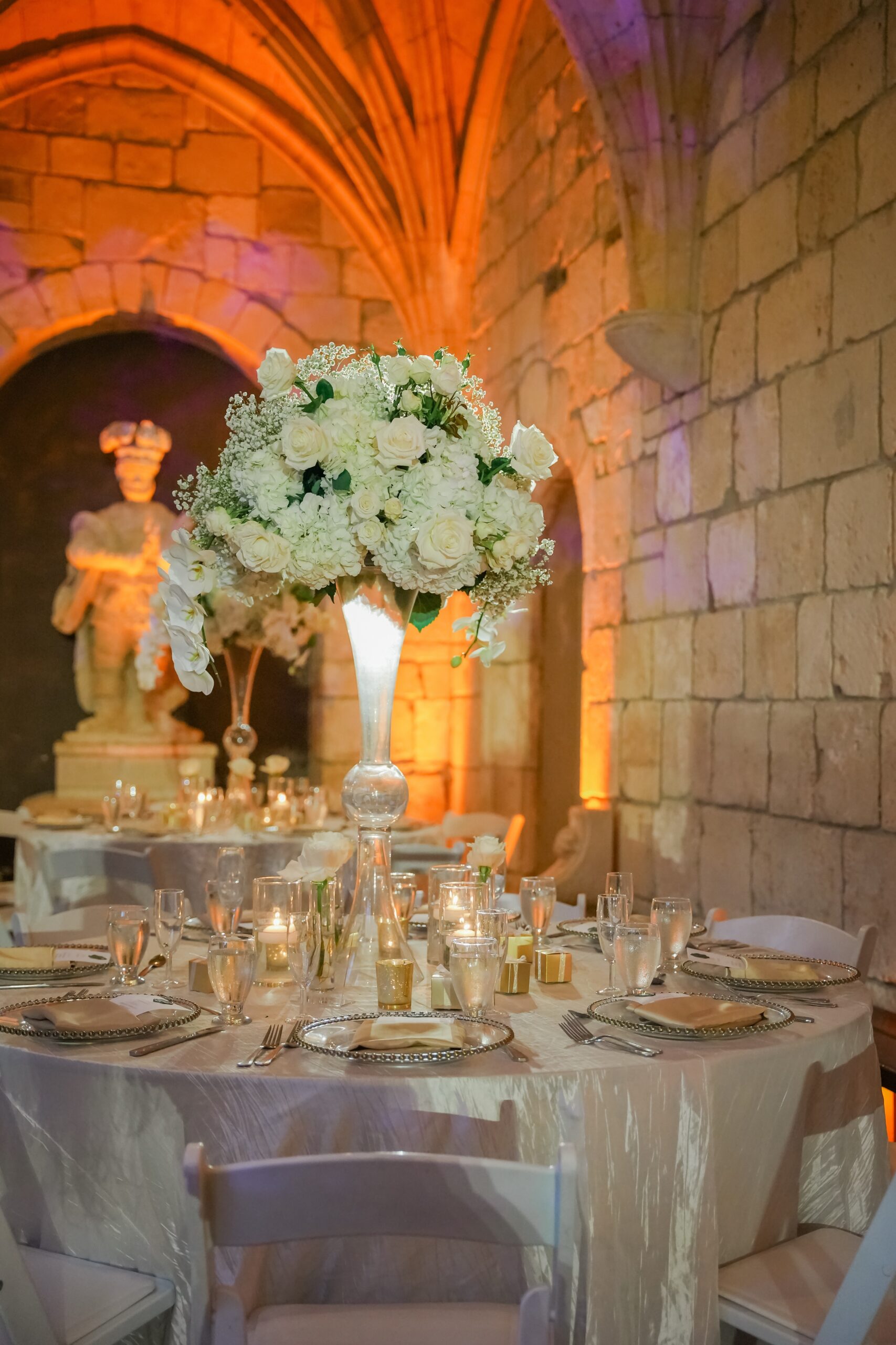 Details of a reception table with white linen and white floral centerpiece at an Ancient Spanish monastery wedding