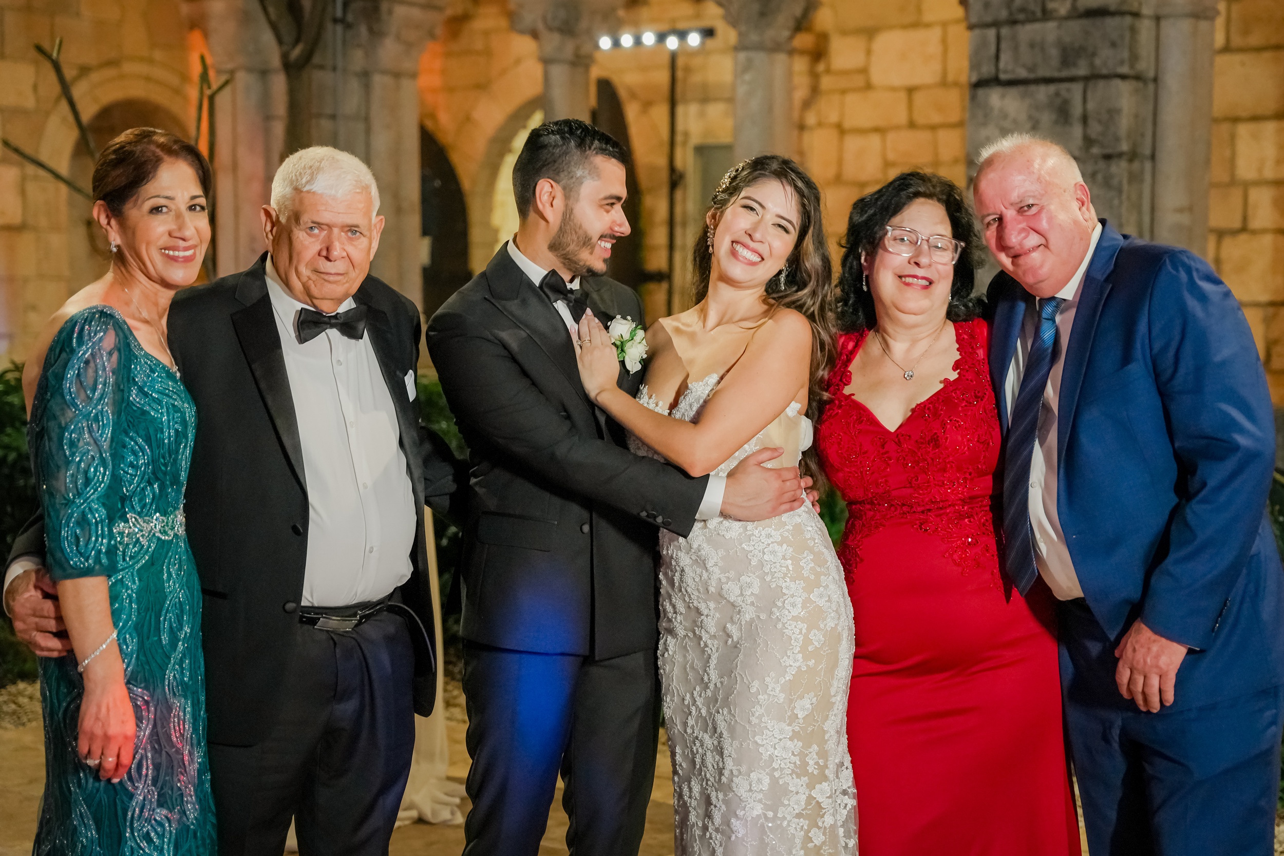 Happy newlyweds smile while standing with their parents in a stone reception space in Ancient Spanish monastery wedding