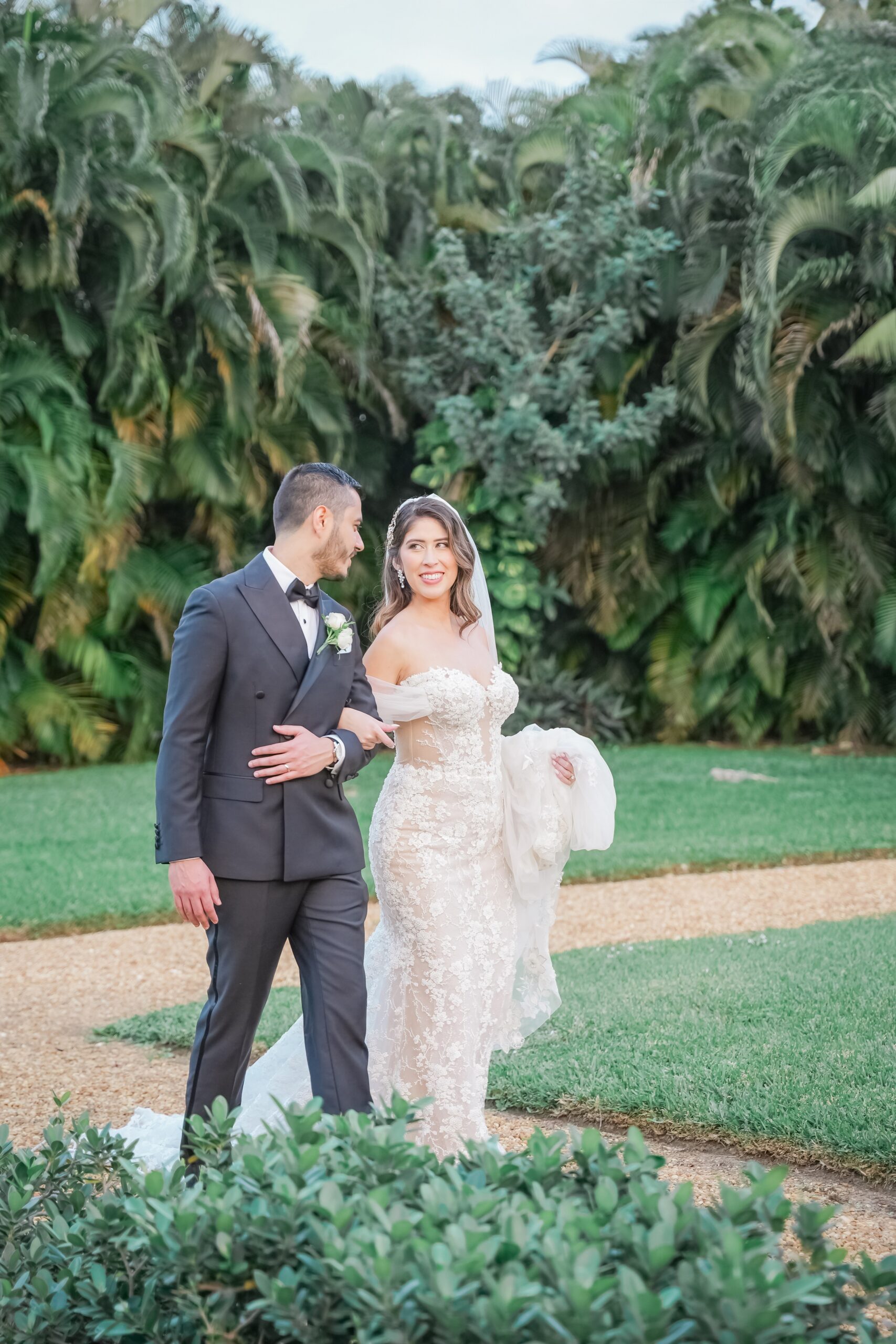 Newlyweds walk a path through a garden locked arms smiling at each other