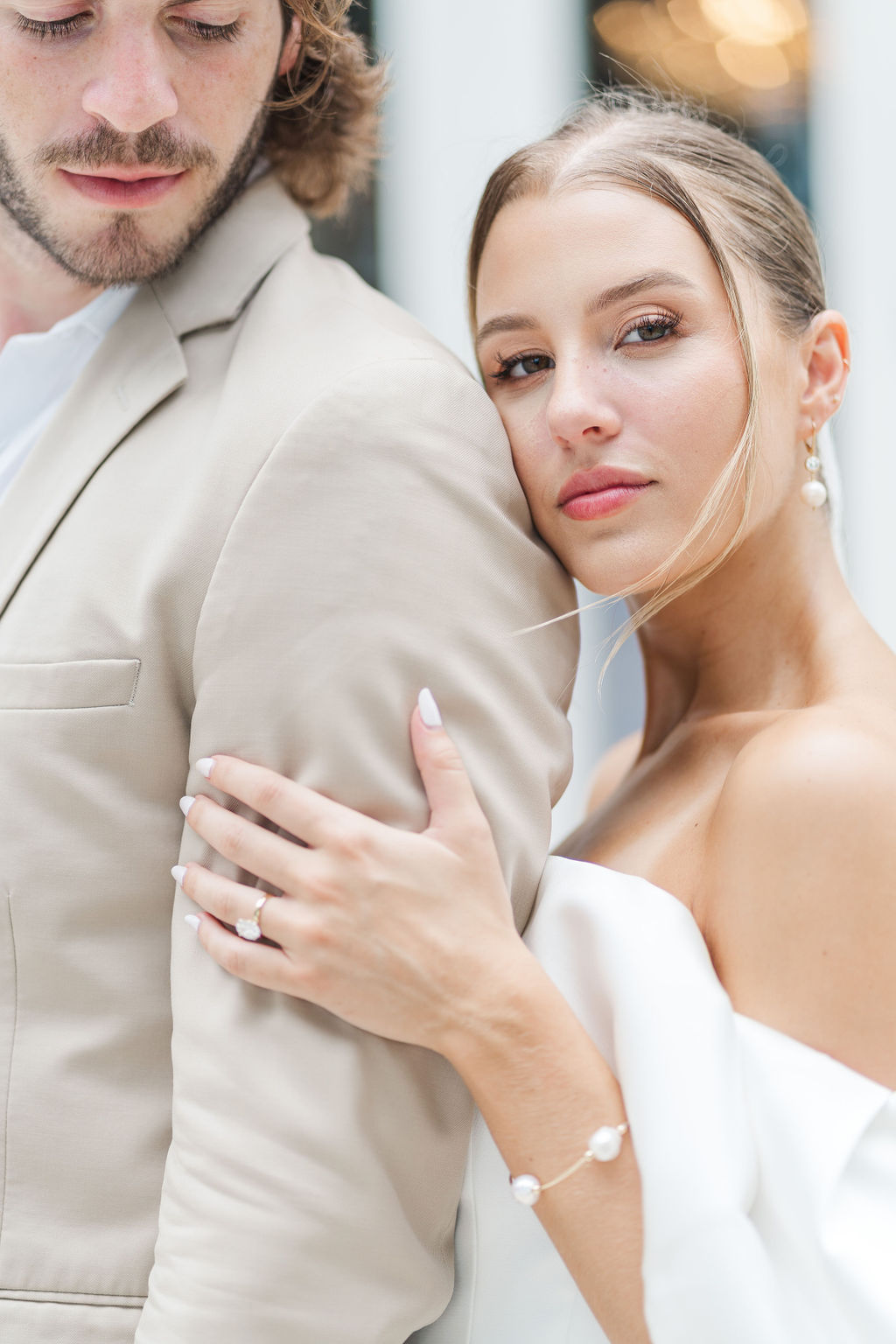 A bride leans on her groom's shoulder in a tan suit