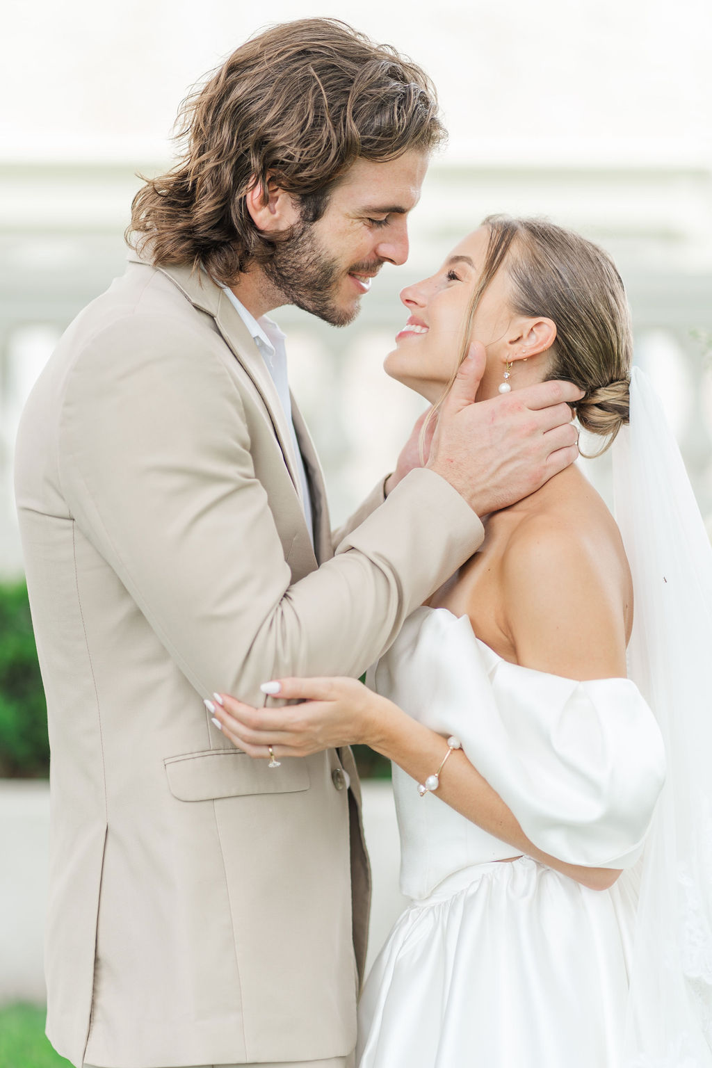 A happy newlywed couple lean in for a kiss in a garden in a tan suit and silk dress