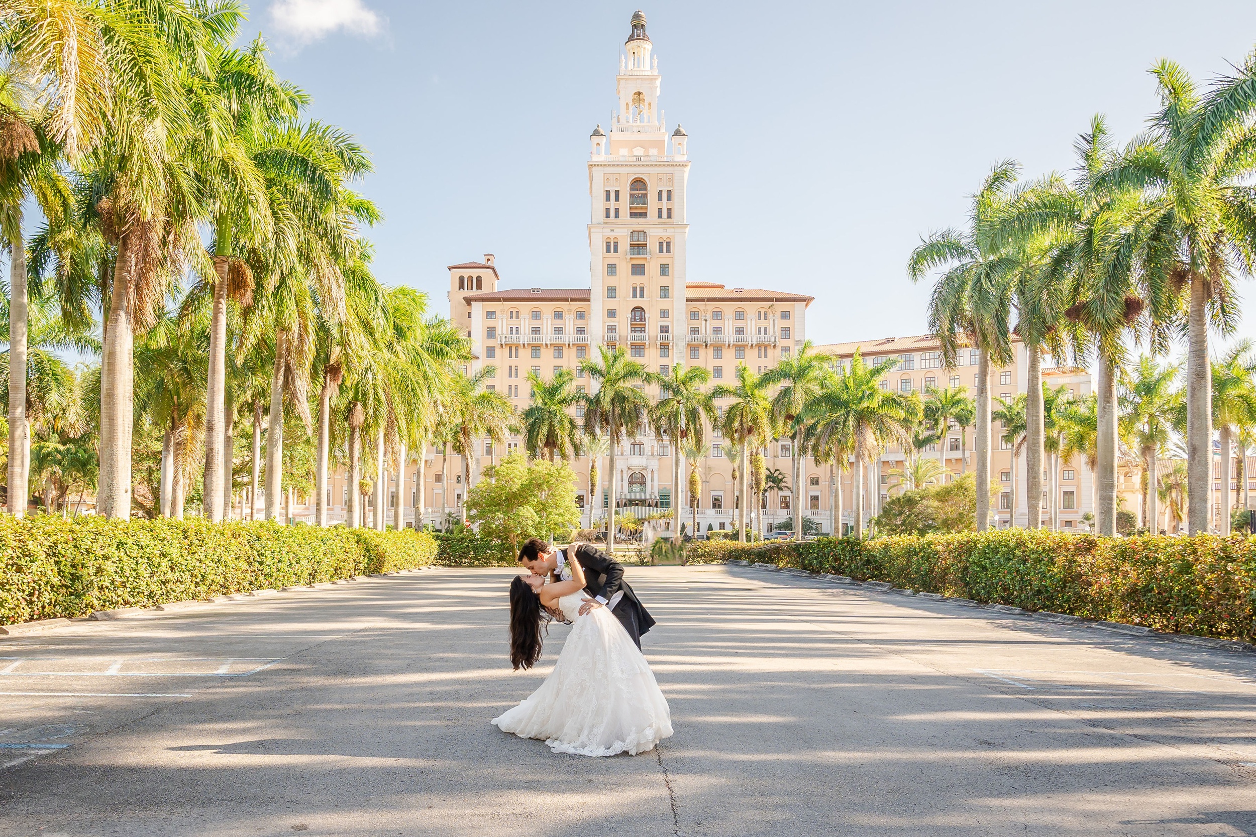 Newlyweds dip and kiss in the palm lined drive in front of one of the luxury wedding venues in miami