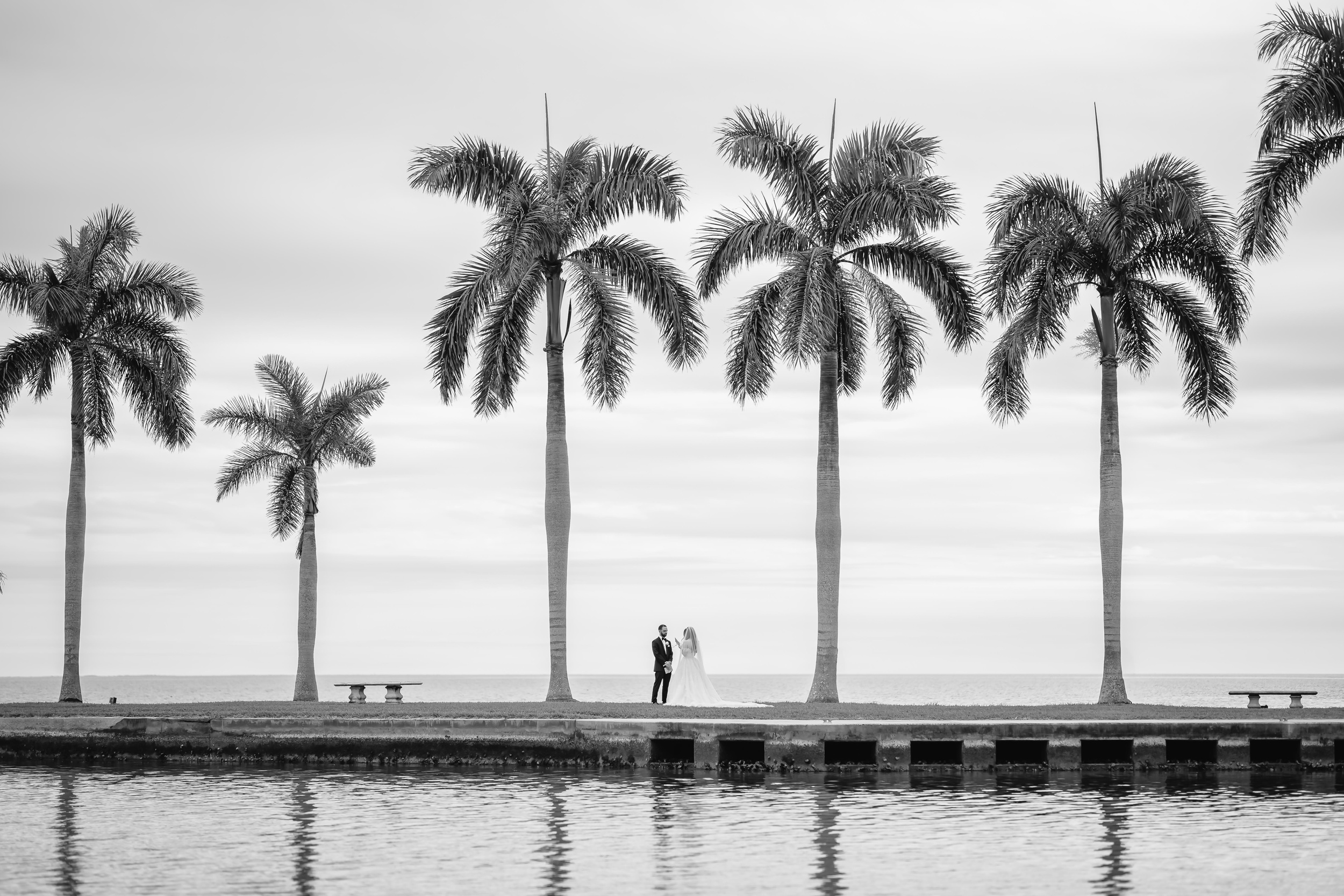 Newlyweds stand on the edge of a large walkway on water's edge at one of the wedding venues in naples florida